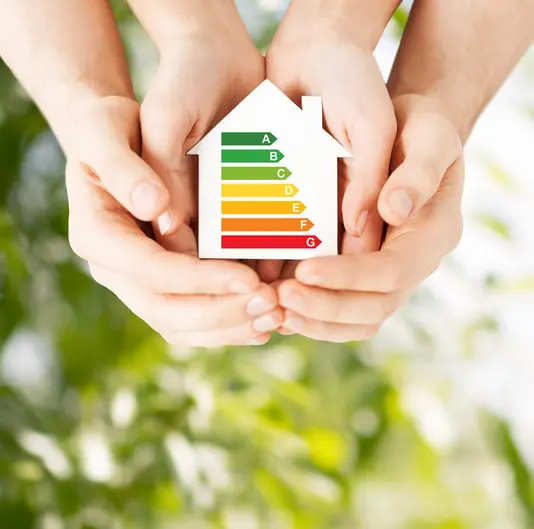 Schützende Hände um ein Energiesparhaus.